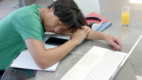 teenage asian boy rests his head on a desk while studying, with copy space