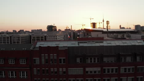 3-Young-People-on-Rooftop-at-Scenic-Golden-Hour-Sunset-above-Berlin,-Germany,-Aerial-Drone-Shot-descending-backwards-dolly-out