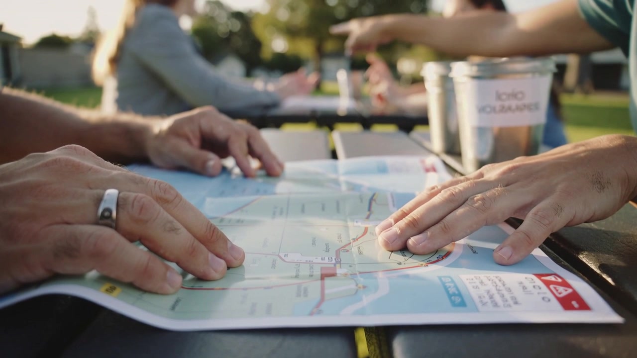 Reacting to pointing gesture, two hands sliding across folded map on park table, planning route