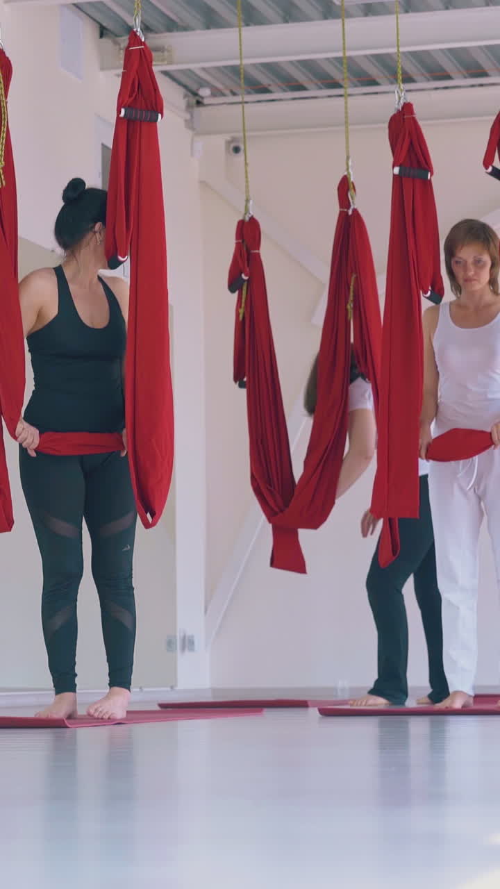 young women group prepares for fly yoga workout with bright red hammocks in new white gym stretching zone
