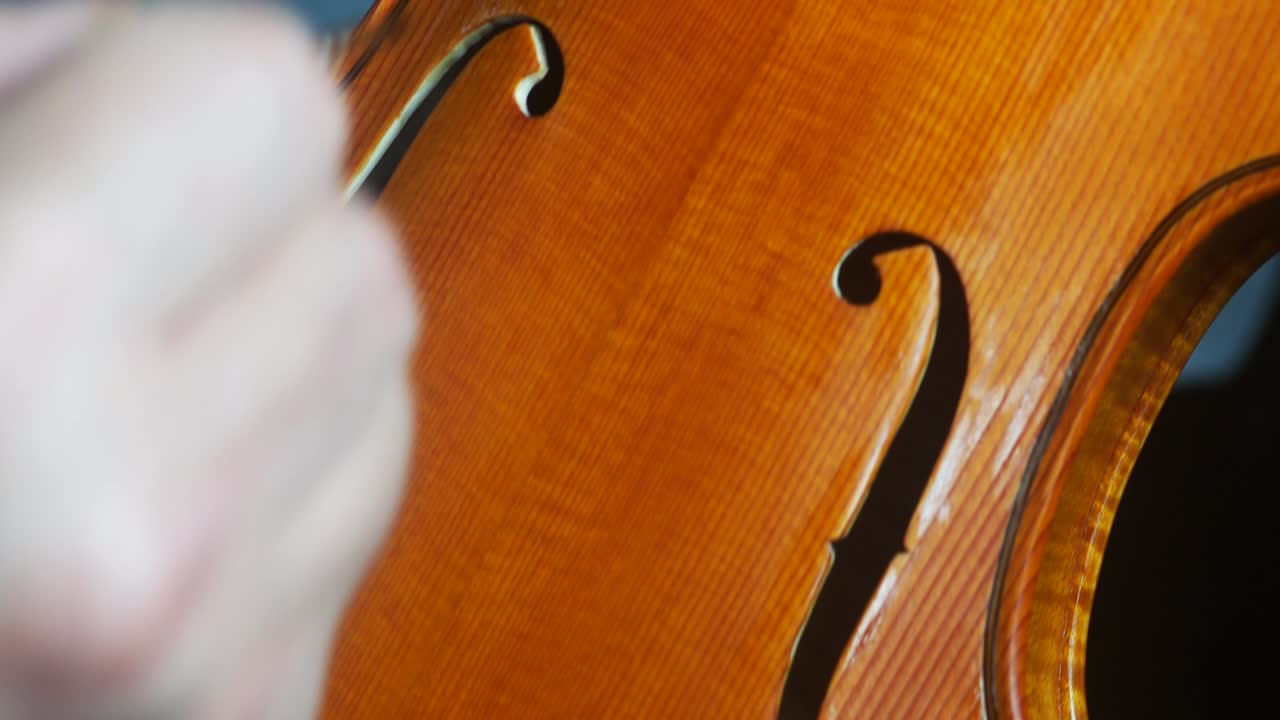 바이올린 제작자 루티에의 손이 손으로 만든 목조 현악기를 바르닝하고 있습니다.