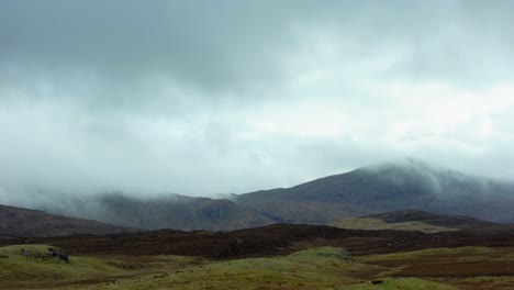 static shot of a cloudy and misty mountain range behind a peatland moor covered in heather