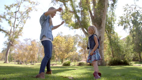 mother and young daughter playing in a park, full length