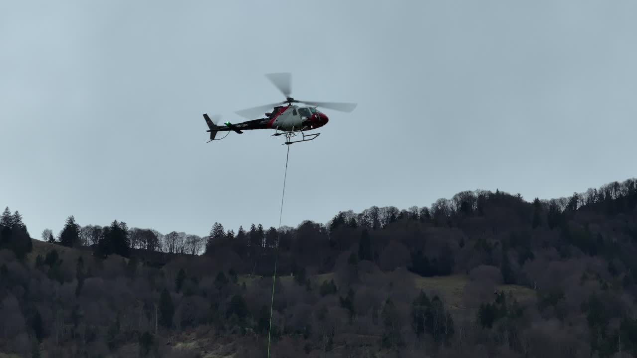 헬리터가 스위스 와이센의 렌세 근처에서 비행을 하고 있는데, 그 배경은 산기?? 에 있는 봄 초기의 울창한 숲입니다.