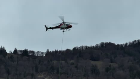 Helicopter-in-flight-near-Walensee,-Weesen,-Switzerland,-with-a-backdrop-of-lush,-early-spring-forests-on-mountain-slopes