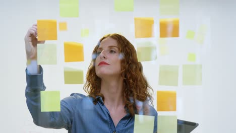 Businesswoman-writing-on-the-sticky-notes-stuck-over-glass-4k