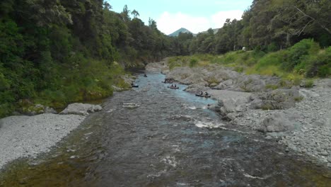 People-paddle-kayak-down-the-rapid-with-rock-boulders-on-beautiful-pristine-clear-blue-Pelours-river,-New-Zealand---Aerial-Drone