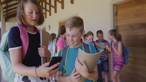 Boy-and-girl-discussing-over-smartphone-in-the-school-corridor