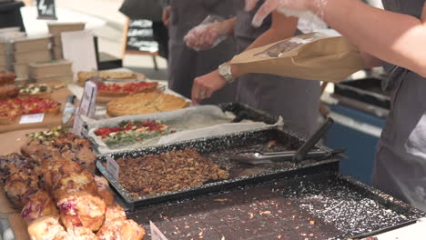 Una-Mujer-Pone-Comida-En-Un-Recipiente,-Un-Festival-De-Comida-En-Las-Calles-De-La-Ciudad,-Productos-Regionales-Probados-Por-La-Gente