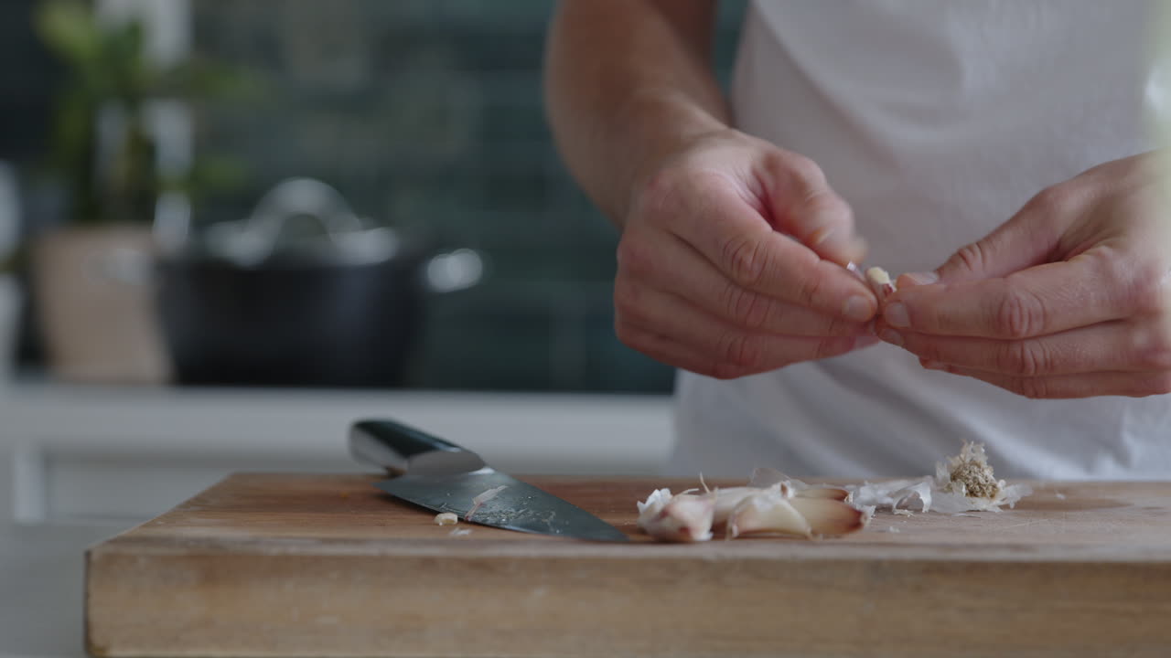 Close-up of a man peeling fresh garlic with his hands in a modern kitchen