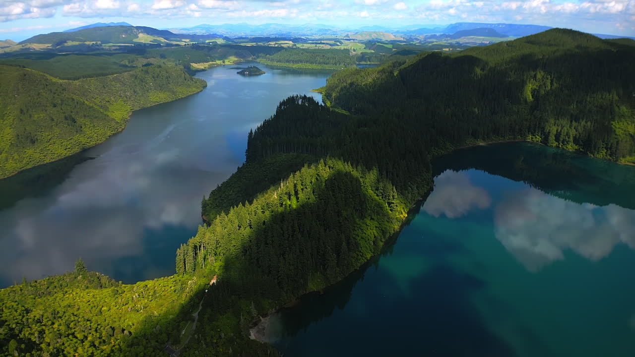 Vista aérea de dois lagos e uma floresta com colinas ondulantes ao longe em um dia parcialmente nublado.