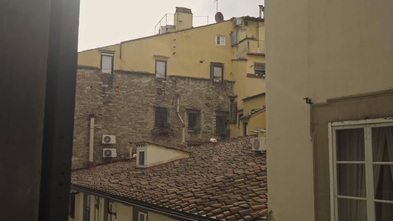 A view overlooking the rooftops and varied architecture of buildings in Florence, Italy. Tiles, brick, and stucco textures are visible.