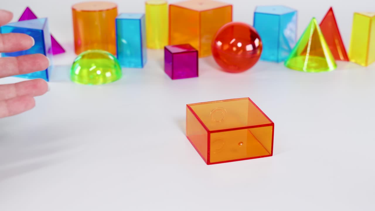 Hands interact with vibrant 3D shapes on a white surface, demonstrating movement and balance in a well-lit environment