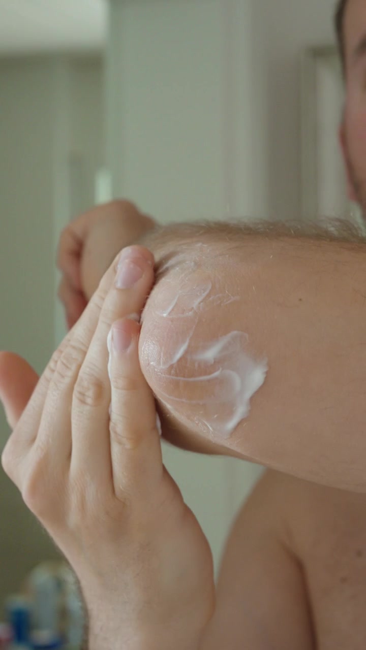 Primer plano de un hombre aplicando crema para el cuidado de la piel en su codo, sugiriendo tratamiento para piel seca, irritación o molestias articulares.