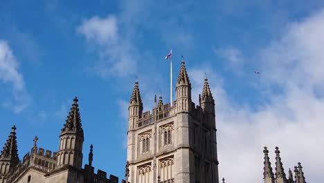 toma en cámara súper lenta de una gaviota volando pasando por la torre de la abadía de bath en somerset, inglaterra, en un día soleado de verano con la cruz de san jorge ondeando en el viento.