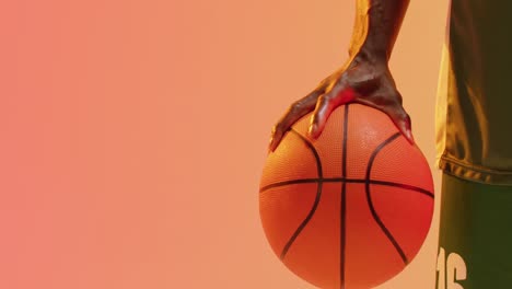 Video-Des-Mittelteils-Eines-Afroamerikanischen-Männlichen-Basketballspielers,-Der-Den-Ball-Auf-Orangefarbenem-Hintergrund-Hält
