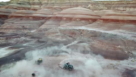 aerial view of man spinning with atv quad in dusty canyon under striped sandstone hills in utah desert, usa