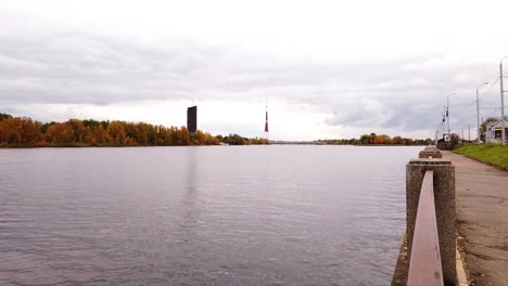 television tower of riga from dauguva river shore with calm and still water in cloudy autumn day