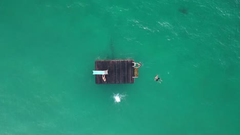 Backflip-dive-into-the-water-from-floating-platform,-aerial-top-down