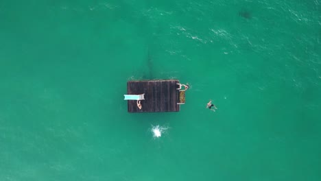 Salto-Hacia-Atrás-En-El-Agua-Desde-Una-Plataforma-Flotante,-Aéreo-De-Arriba-Hacia-Abajo