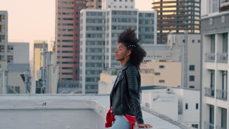 slow motion beautiful young african american woman relaxing on rooftop with confidence enjoying glamorous urban lifestyle wind blowing hair in city background