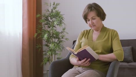 senior woman with gray hair sitting on a sofa reading a book