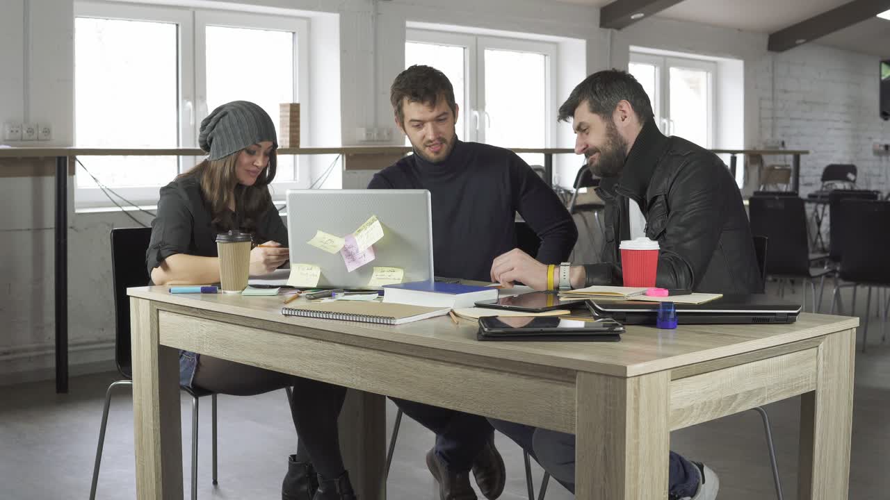 Team of young professionals having a meeting in a creative office. Business discussion. Coffee cups and laptop on the table. Shot in 4k