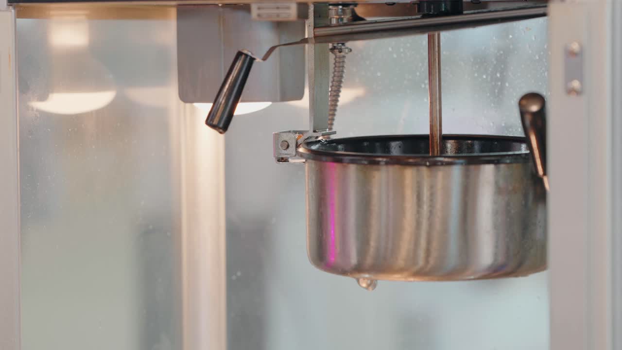 팝콘 기계 안의 뜨거운, 증기 있는 팝콘 팬의 클로즈업, 손잡이가 보입니다.