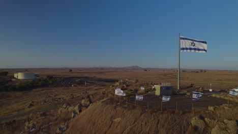 the israeli flags as a memorial to idf soldiers who were killed in the war against syria, they are in the golan heights with many wind turbines for electricity production in the background