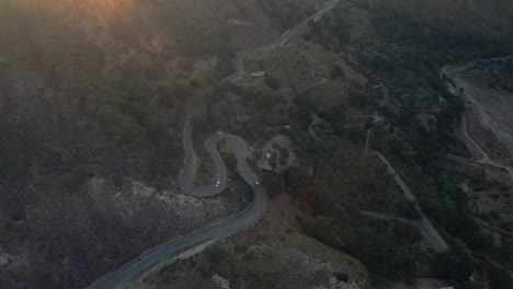 aerial shot circling around two cars as they traverse the winding turns of a mountain pass in southern italy