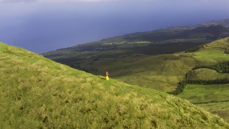 asian malaysian chinese tourist woman making video or photo with phone on a path on the edge of the vulcanic green mountain, drone view on pico da esperança, in são jorge island, the azores, portugal