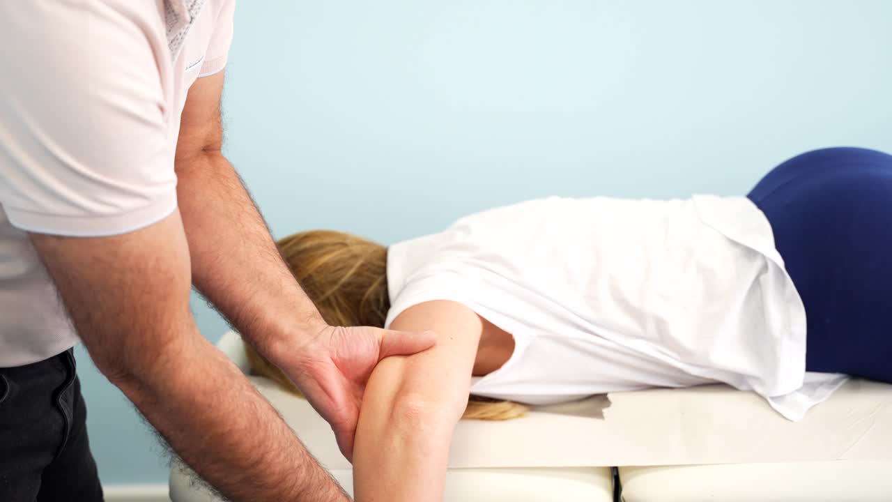 Physiotherapist correcting arm of woman on massage table