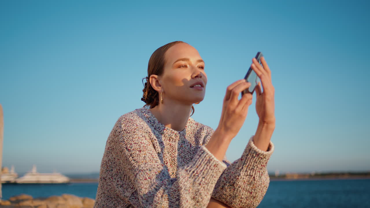 modelo de mar grabando video en la orilla al atardecer en primer plano. niña hermosa descansando al aire libre