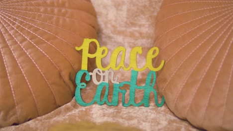 cool vintage retro shot of a sign saying peace on earth which is placed on a couch in between pink orange pillows slow motion unique scene