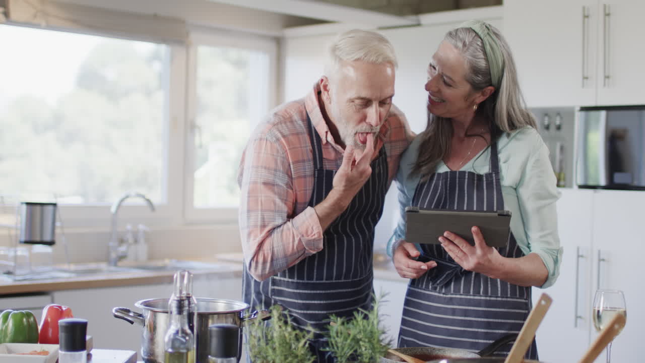 pareja caucásica de mediana edad usando tableta, preparando comida, cocinando en la cocina en casa, cámara lenta