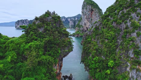 aerial drone flying through a gap of limestone rocks along phra nang beach in railay, thailand