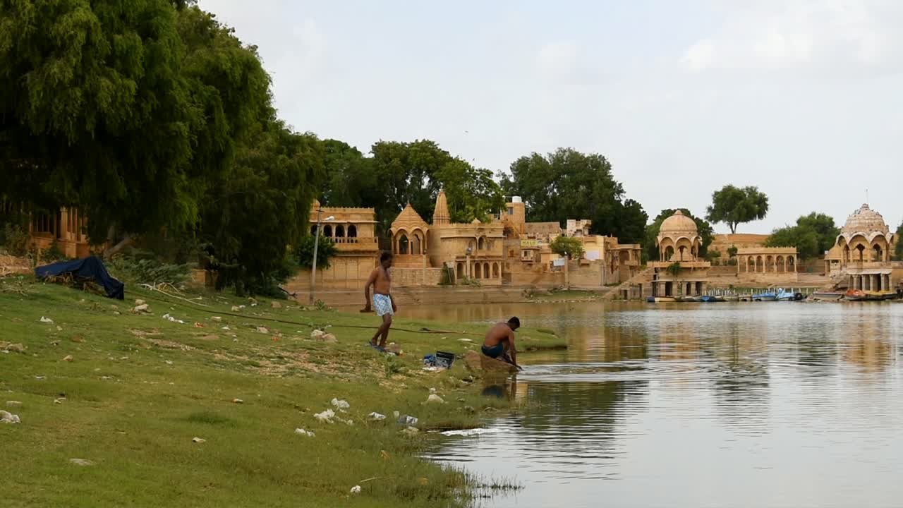 two poor local men bathing and washing clothes at the shore of lake