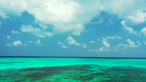 Bright-sky-with-big-white-clouds-hanging-over-turquoise-lagoon-with-beautiful-patterns-of-coral-reefs-on-a-tropical-scenery-in-Bora-bora