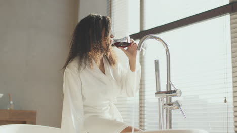 woman relaxing in a modern bathroom with a glass of red wine