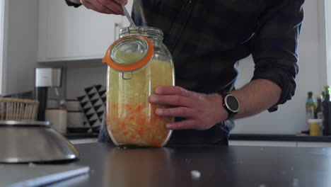 medium shot of person fermenting food in glass jar at home kitchen