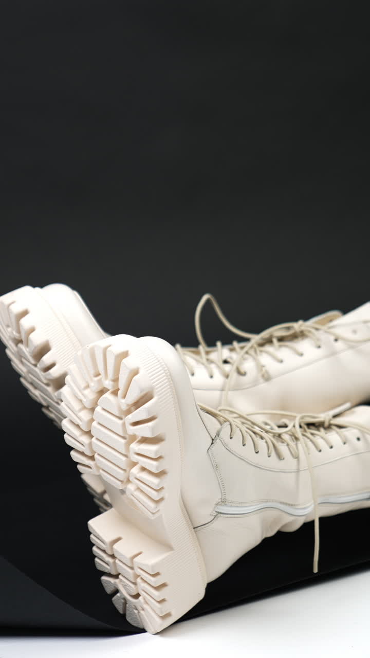 Legs of a model wearing white tractor soles boots. Female sitting on the floor in studio demonstrating modern stylish footwear. Vertical video