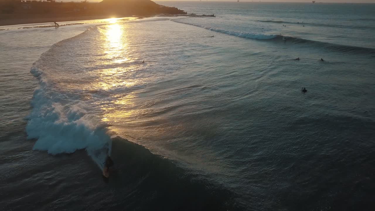 Drone aerial view of a surfer catching a long wave during sunset in South america