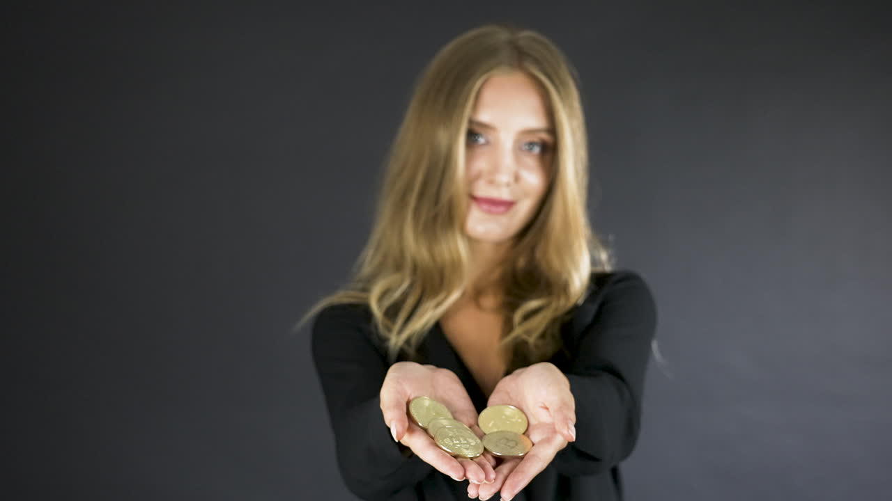 joven rubia muestra monedas de criptomonedas de oro en sus palmas
