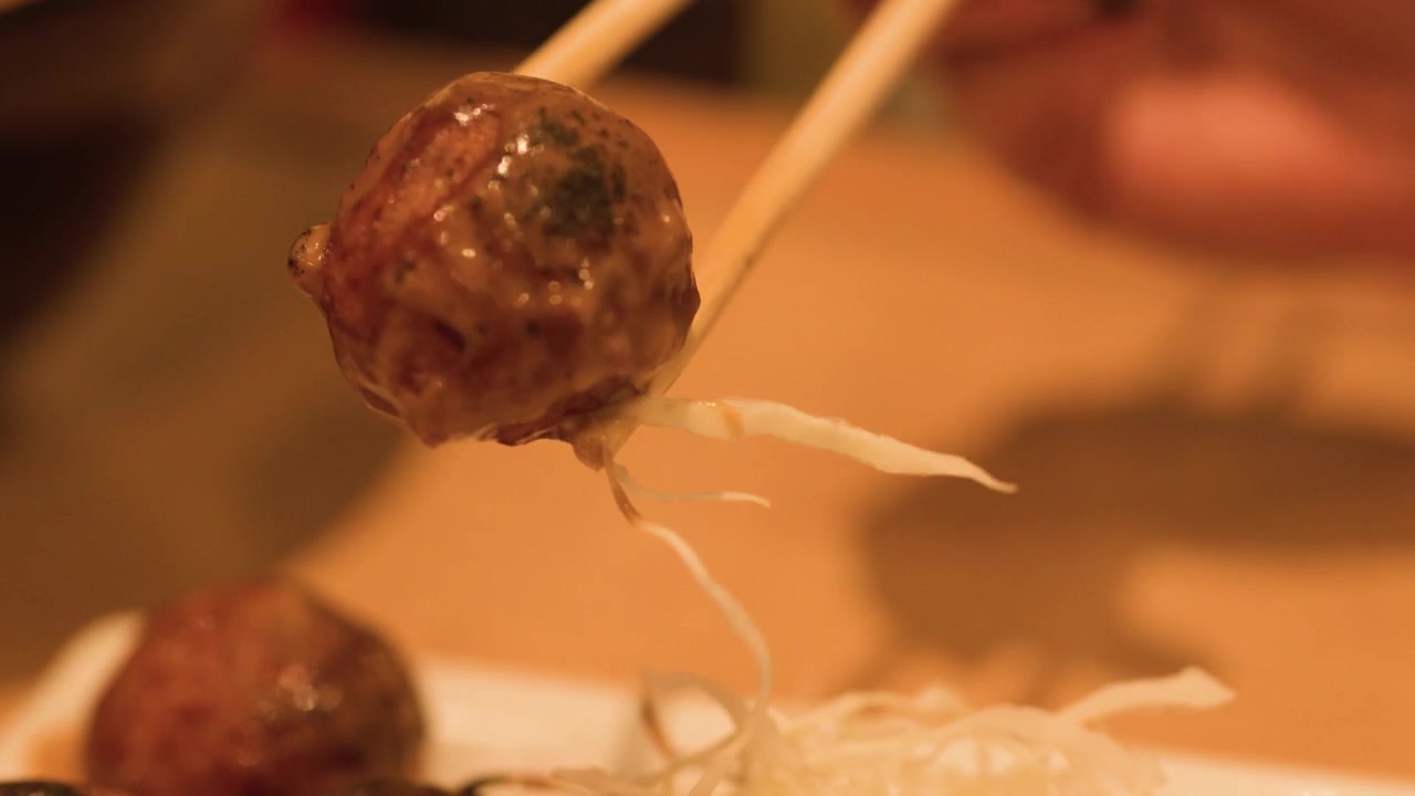 Primo piano di bacchette che sollevano una pallina di takoyaki glassata da un piatto con cavolo cappuccio sminuzzato