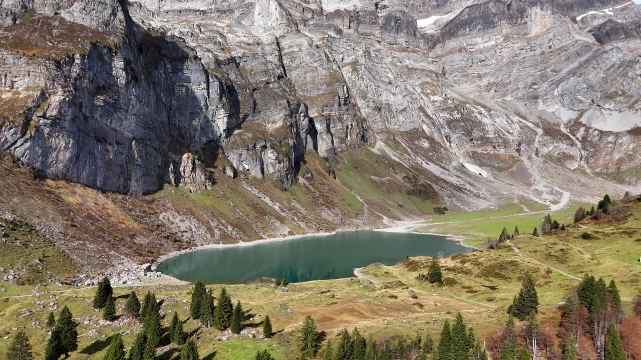 Serene alpine lake surrounded by rugged cliffs and green meadows in Switzerland
