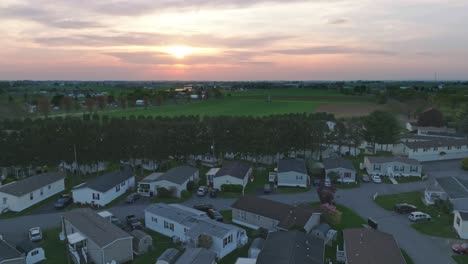 A-tranquil-suburbia-basks-under-a-dusky-sky-as-the-sun-dips-low,-casting-a-warm-glow-over-neatly-aligned-mobile,-prefab,-manufactured,-homes