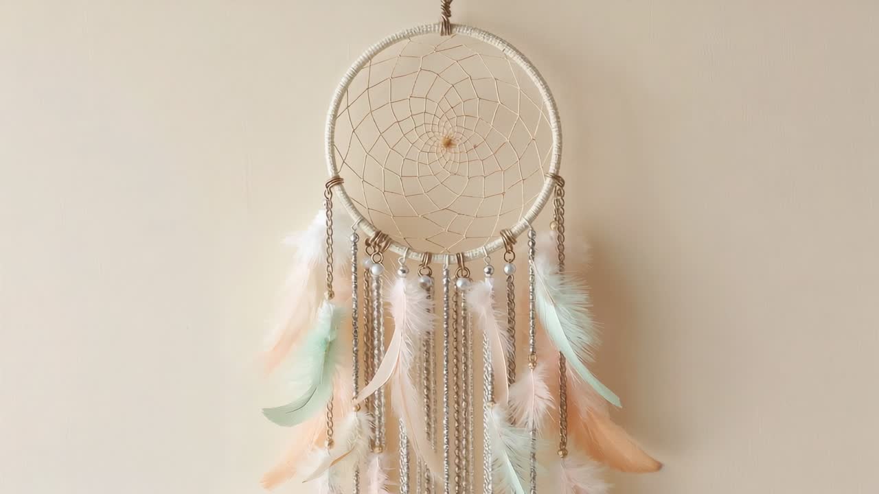 Subtle breeze driving dreamcatcher swaying against pale beige wall with feathers and metal chains