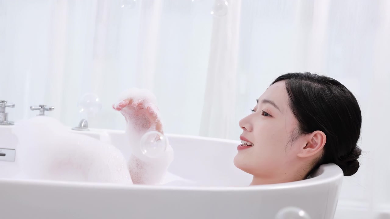 Attractive elegant seductive woman blowing foam while relaxing in hot bath with bubbles, enjoying luxury bathroom romantic happy girl taking bathtub plays blowing on foam perfect skin care.