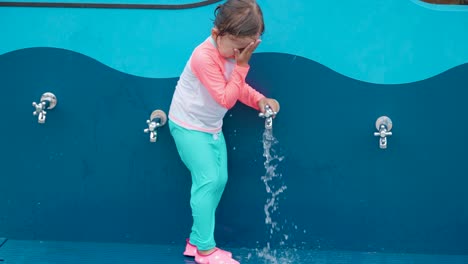 Niña-Pequeña-En-Traje-De-Baño-Se-Lava-La-Cara-De-La-Arena-En-La-Playa-Pública-Afuera