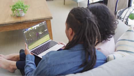 video de dos personas afroamericanas sentadas en el sofá y viendo un partido de fútbol en una computadora portátil